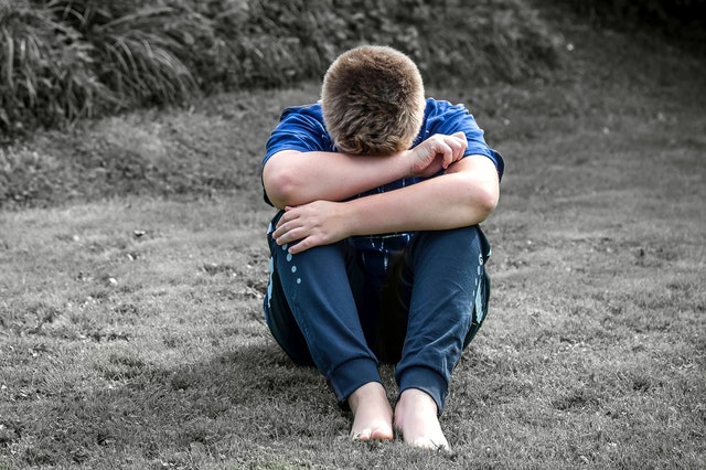 upset child outdoors with head in knees