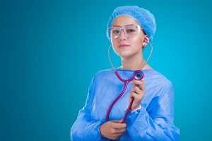 stock image of young woman in surgical scrubs holding a stethoscope in a teal background