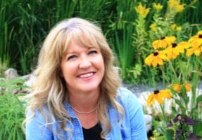 Headshot of Traci Rock outdoors sitting next to blooming flowers