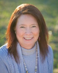 Photo of Vicki Tucker outdoors while wearing a light purple sweater and a beaded necklace