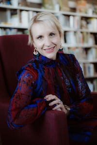 Nicole Woodman's professional headshot while sitting on a burgundy chair in front of a bookcase