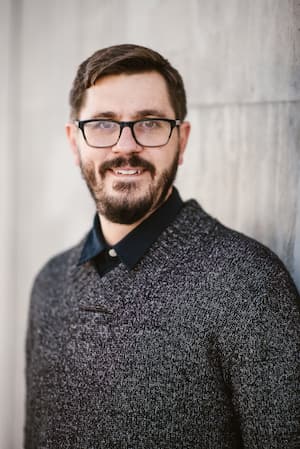 Online therapist Mark Pennick wearing a gray sweater standing by a beige wall