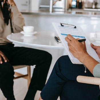 Stock photo of therapist and client siting at table therapist holding a clipboard