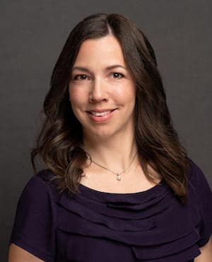 Laura Hundemann's professional headshot wearing a black top in front of dark background.